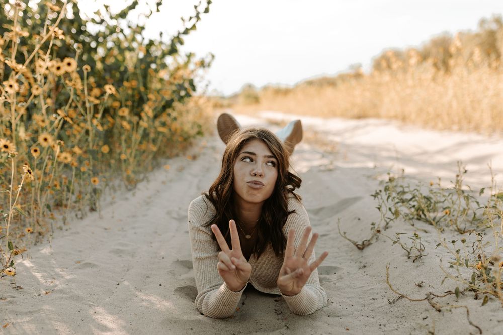 Playful portrait taken while laying in sand near blooming yellow flowers.