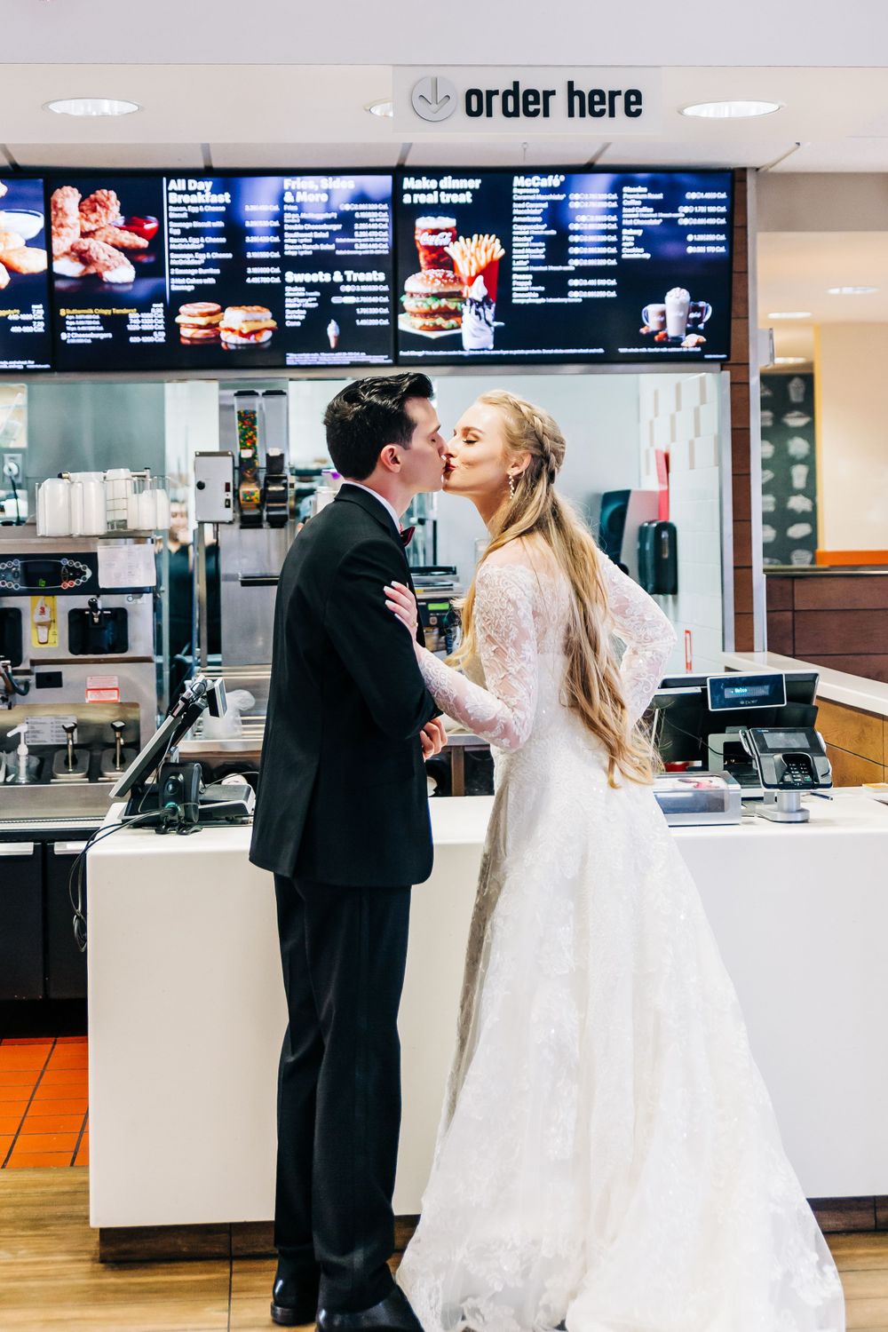 Bride and groom share romantic kiss in front of fast food restaurant counter.