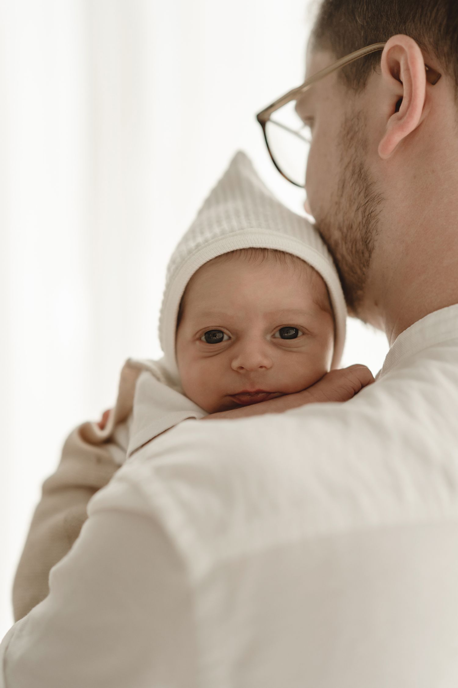 Gentle indoor portrait showing nurturing parental moment in soft natural light.