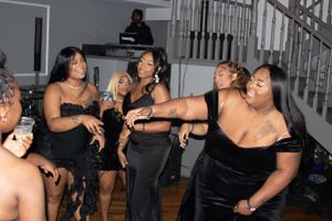 Partygoers in black dresses dancing and socializing at an indoor celebration event.