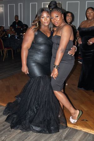 Two friends in black evening wear share a moment together at a formal party.