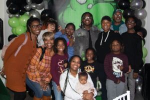 Large group gathered for a photo at an event with green backdrop and balloon decorations.