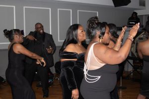 Group of party guests dancing and having fun at an indoor celebration wearing black outfits.