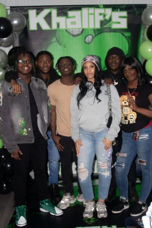 Group photo of attendees posing together at event with green backdrop and balloon decorations.