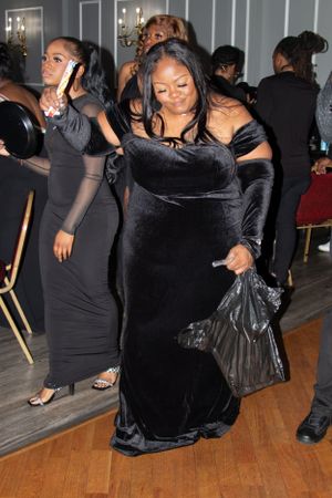 Guests in formal black attire dancing and mingling on hardwood floors at an event.