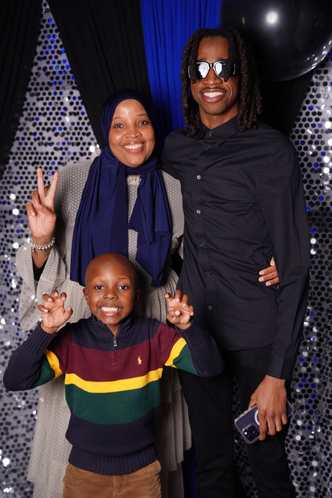 A family poses together against a sparkly backdrop making peace signs.