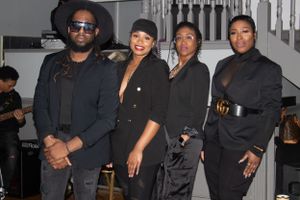 Group in all-black attire posing together in front of stairs at formal event.