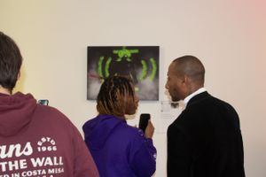 Three people engaged in conversation at an event with green artwork in background.