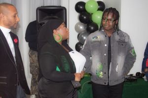 People having a conversation at an event with green and black balloon decorations visible.