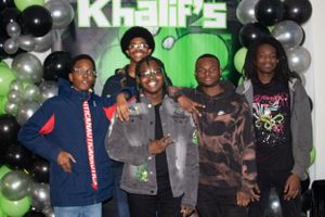 Group of friends posing together against green backdrop with black and silver balloon decorations.