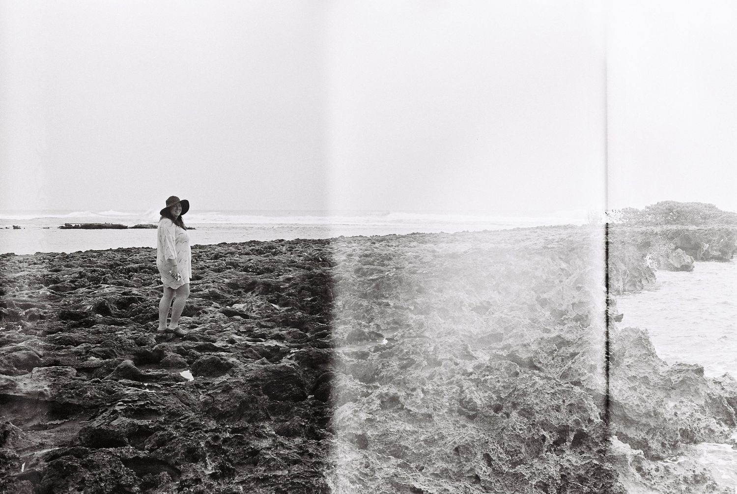 Black and white photograph of a figure standing on rocky terrain near the ocean.