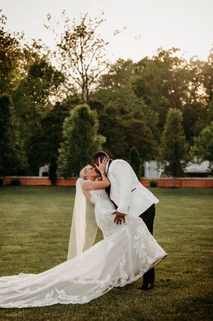 Bride and groom sharing a romantic dip kiss on a green lawn at golden hour during their wedding.