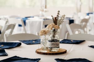 Rustic wedding centerpiece with dried flowers in mason jars on wood slice with navy blue napkins.