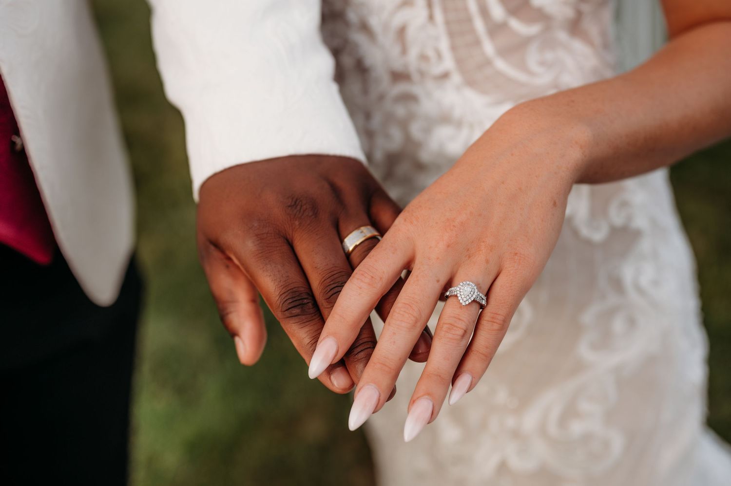 Close-up of interracial newlywed couple holding hands displaying wedding rings and a diamond engagement ring.