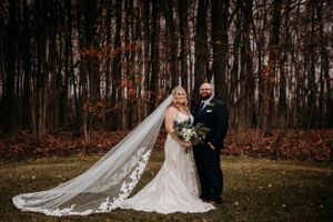 Bride and groom portrait in autumn forest with long lace cathedral veil trailing behind.