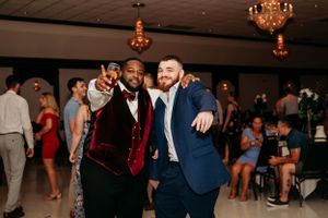 Two men smile and pose together on the dance floor during a lively wedding reception celebration.