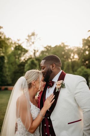 Bride and groom sharing an intimate moment outdoors, groom wearing white tuxedo with burgundy accents.