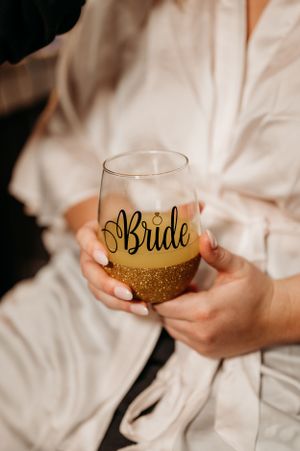Bride holds gold glitter stemless wine glass with Bride script during wedding morning prep.