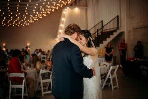 Bride and groom share first dance in warmly lit wedding reception venue with string lights.