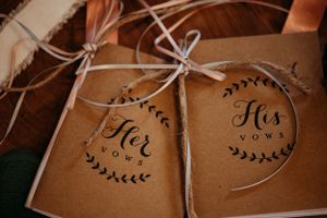 Rustic kraft paper His and Her vows booklets tied with ribbon bows for wedding ceremony.