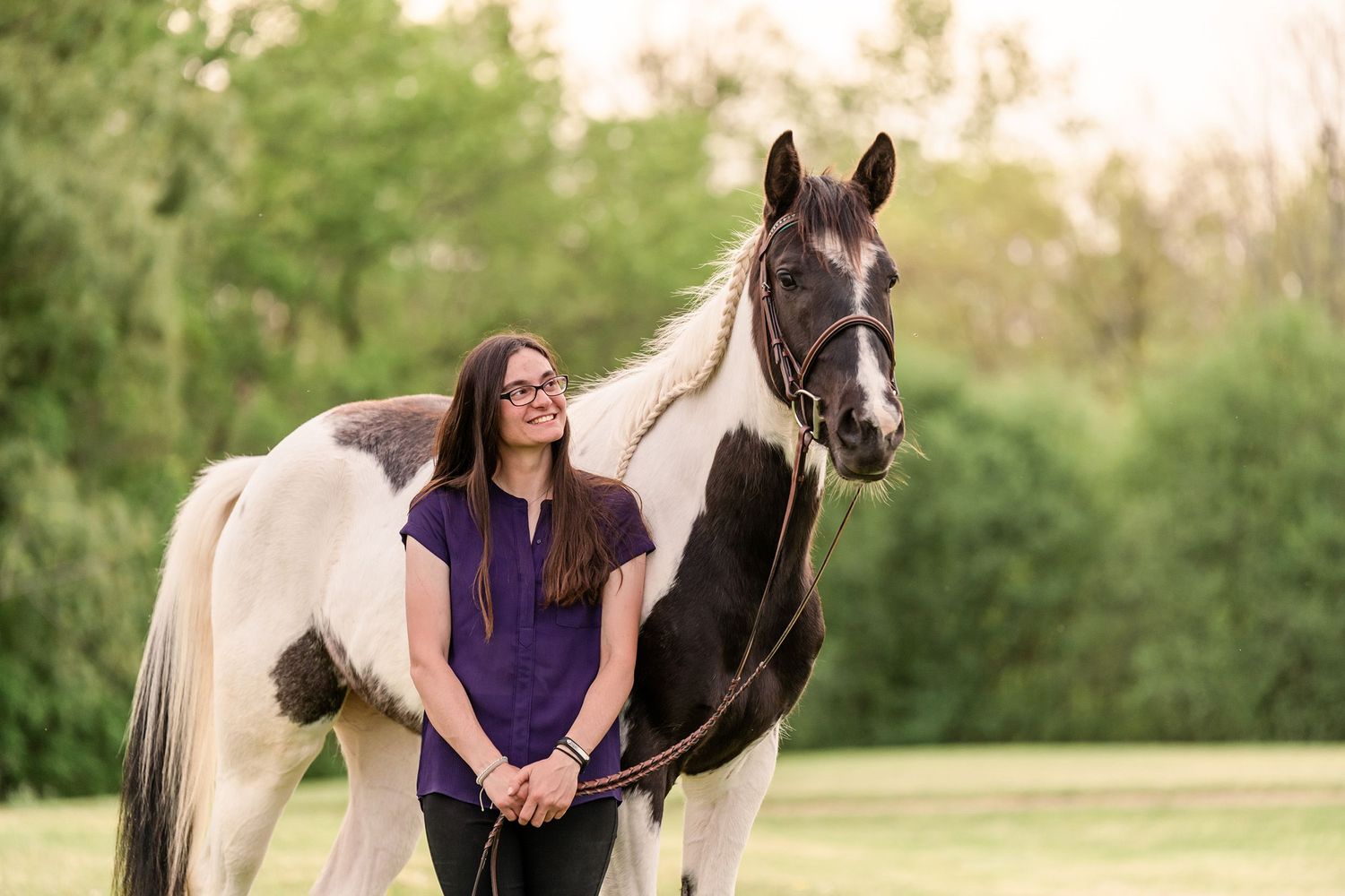 Girl in purple shirt smiling at black and white paint horse