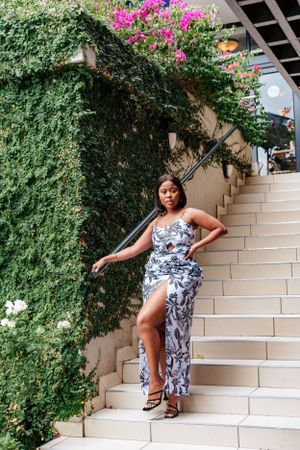 Floral print maxi dress photographed against stone steps and climbing vines with pink flowers.