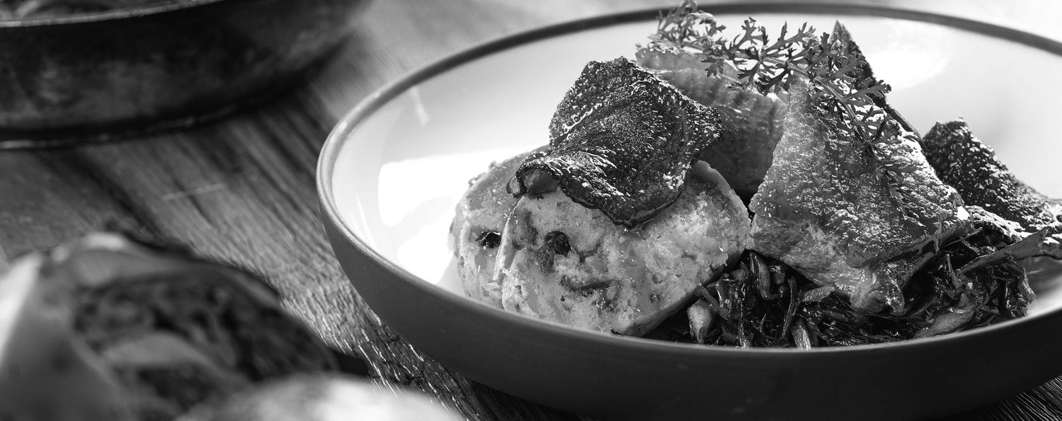Black and white close-up of a gourmet meat dish served in a bowl.