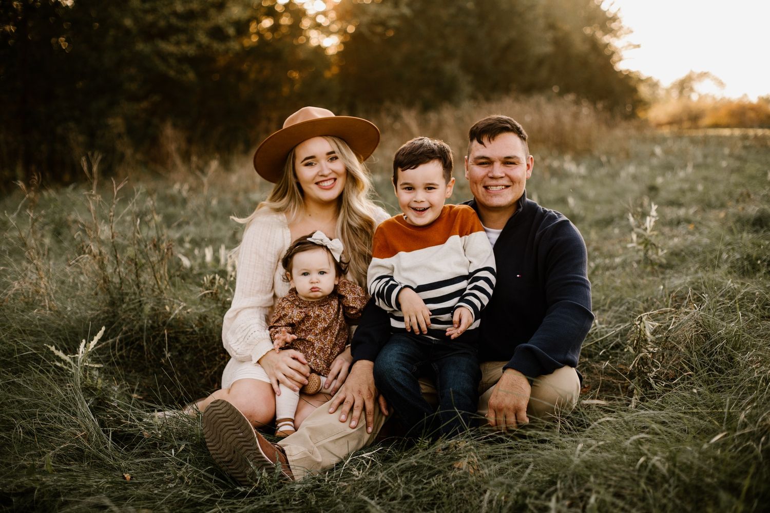Family sitting together in tall grass during golden hour sunset photography session.