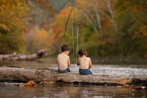 two little boys sit on log in river fishing