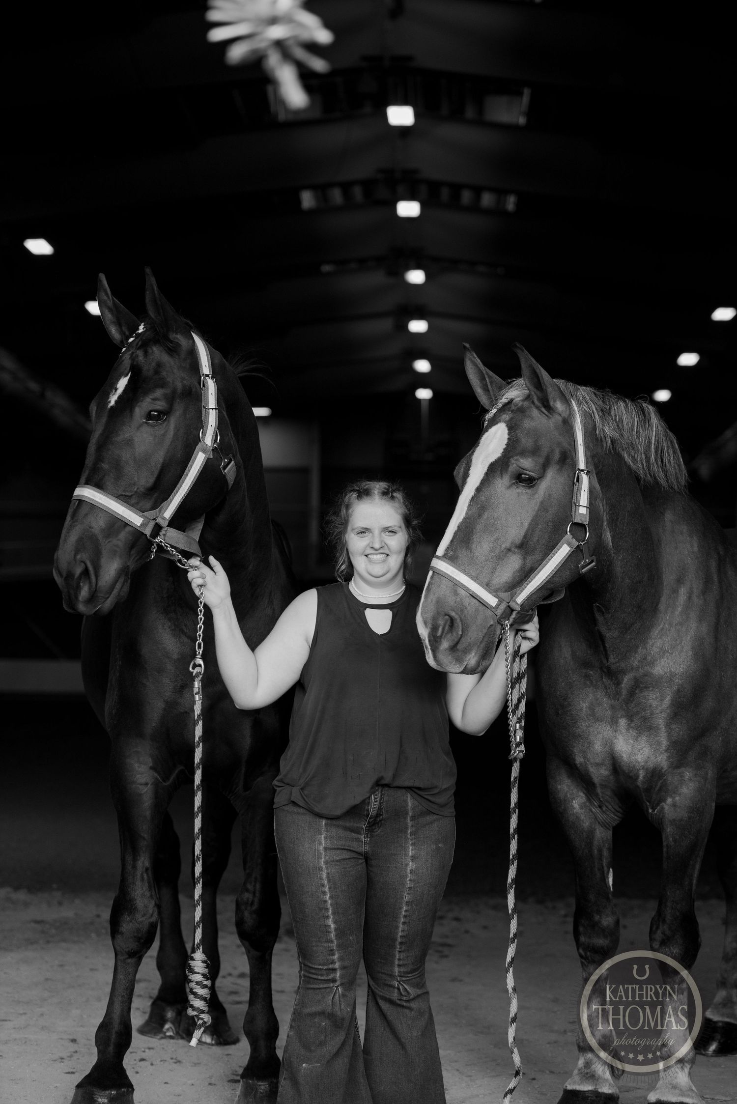 Black and white photo of two horses with halters standing in an indoor arena.
