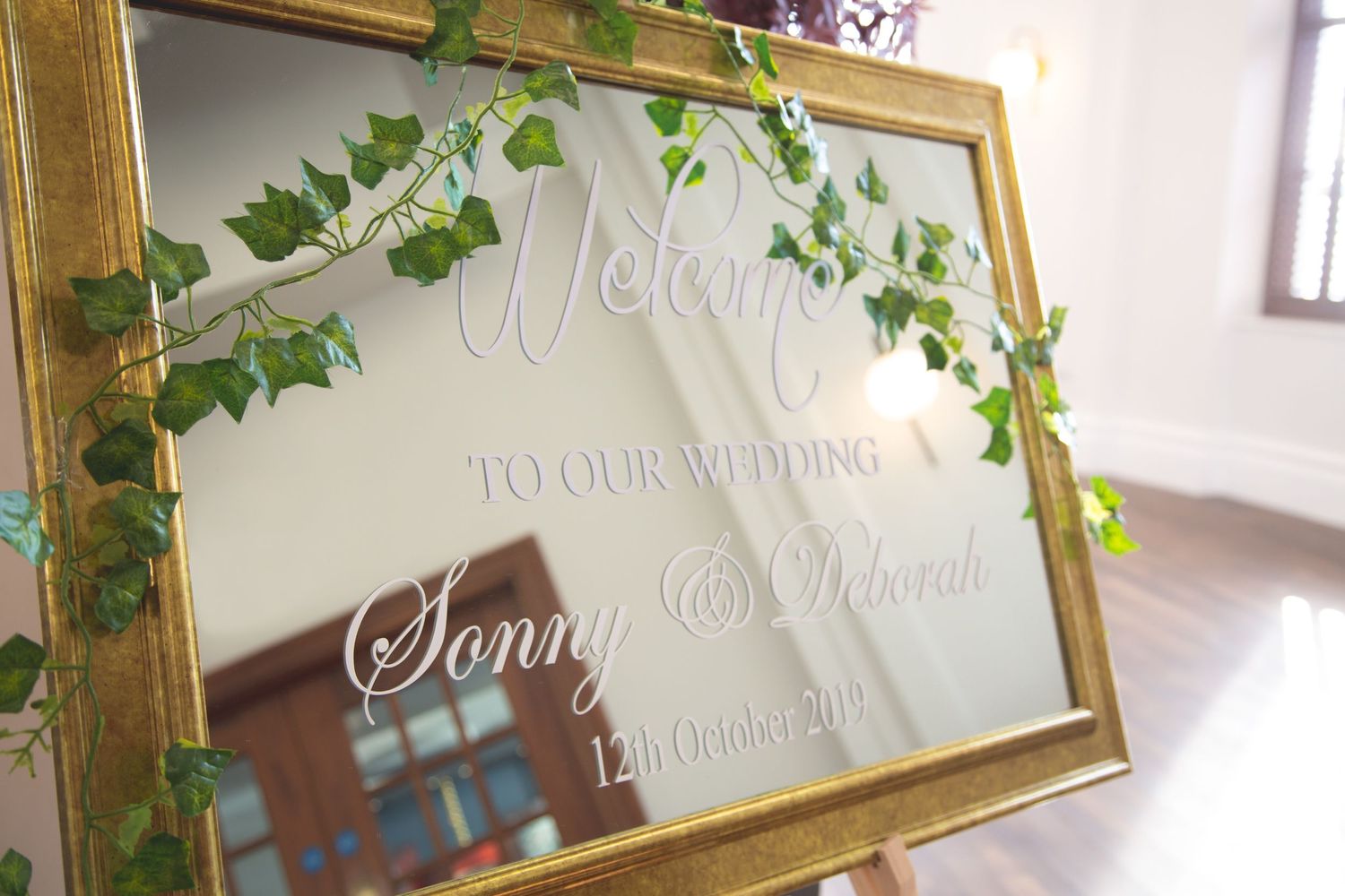 Decorative welcome sign in gold frame with ivy accents for wedding reception.