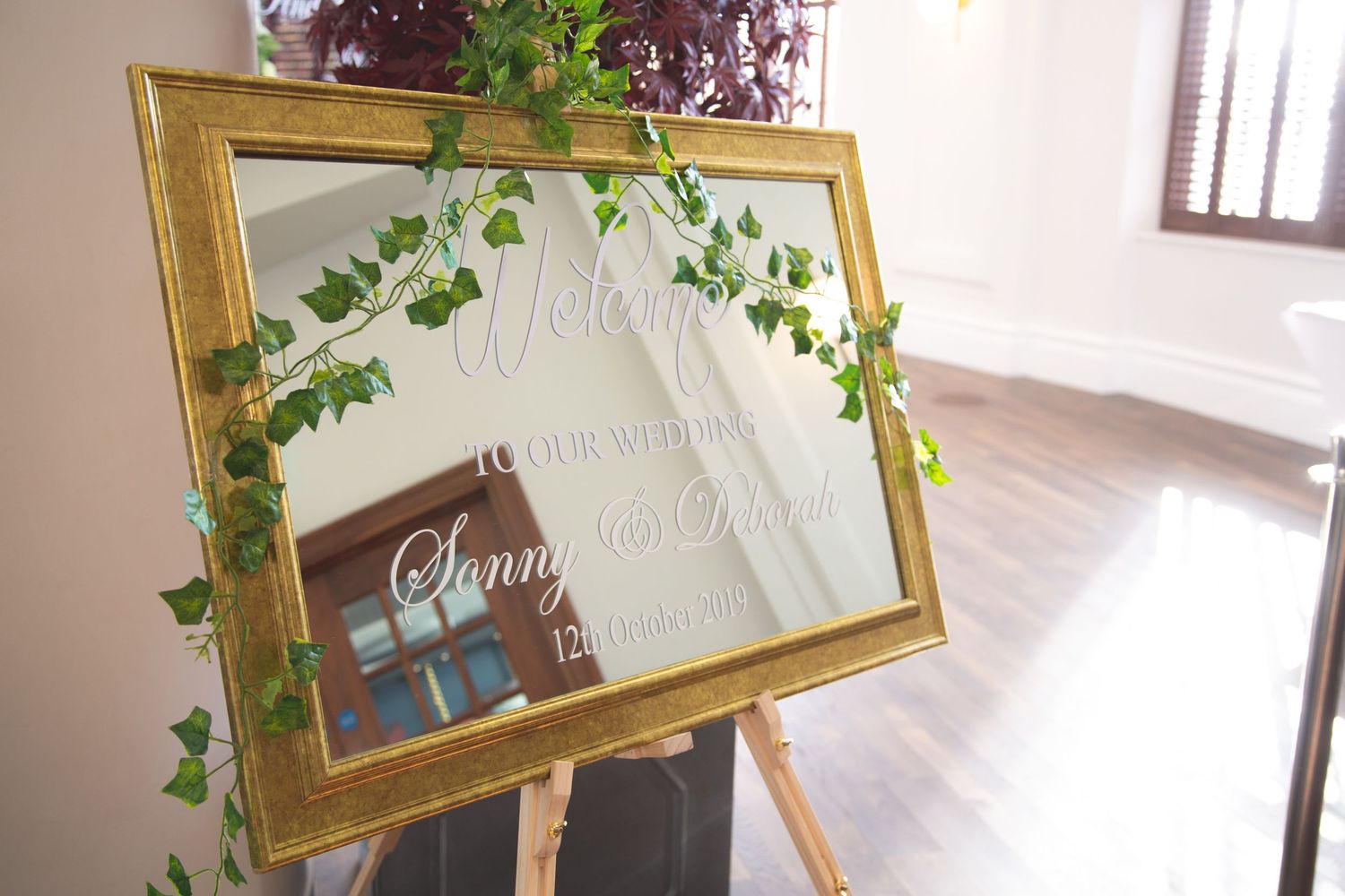 Elegant gold-framed wedding welcome mirror decorated with green ivy vines.