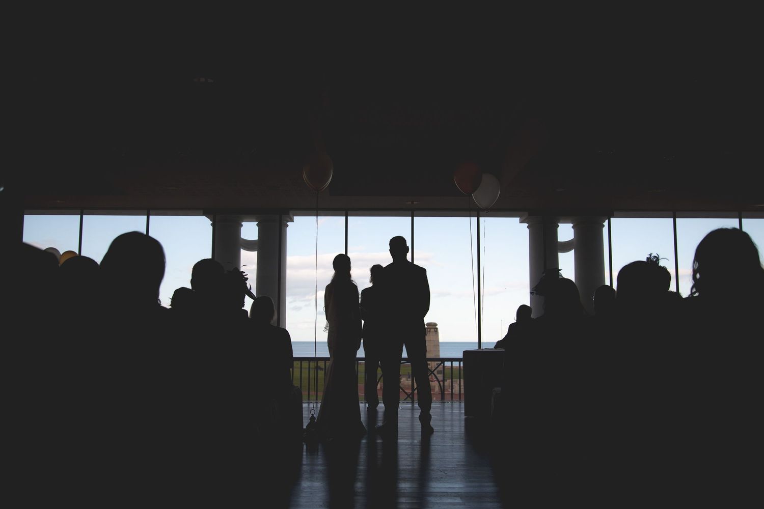 Silhouettes of people standing by large windows looking out at bright daylight view.