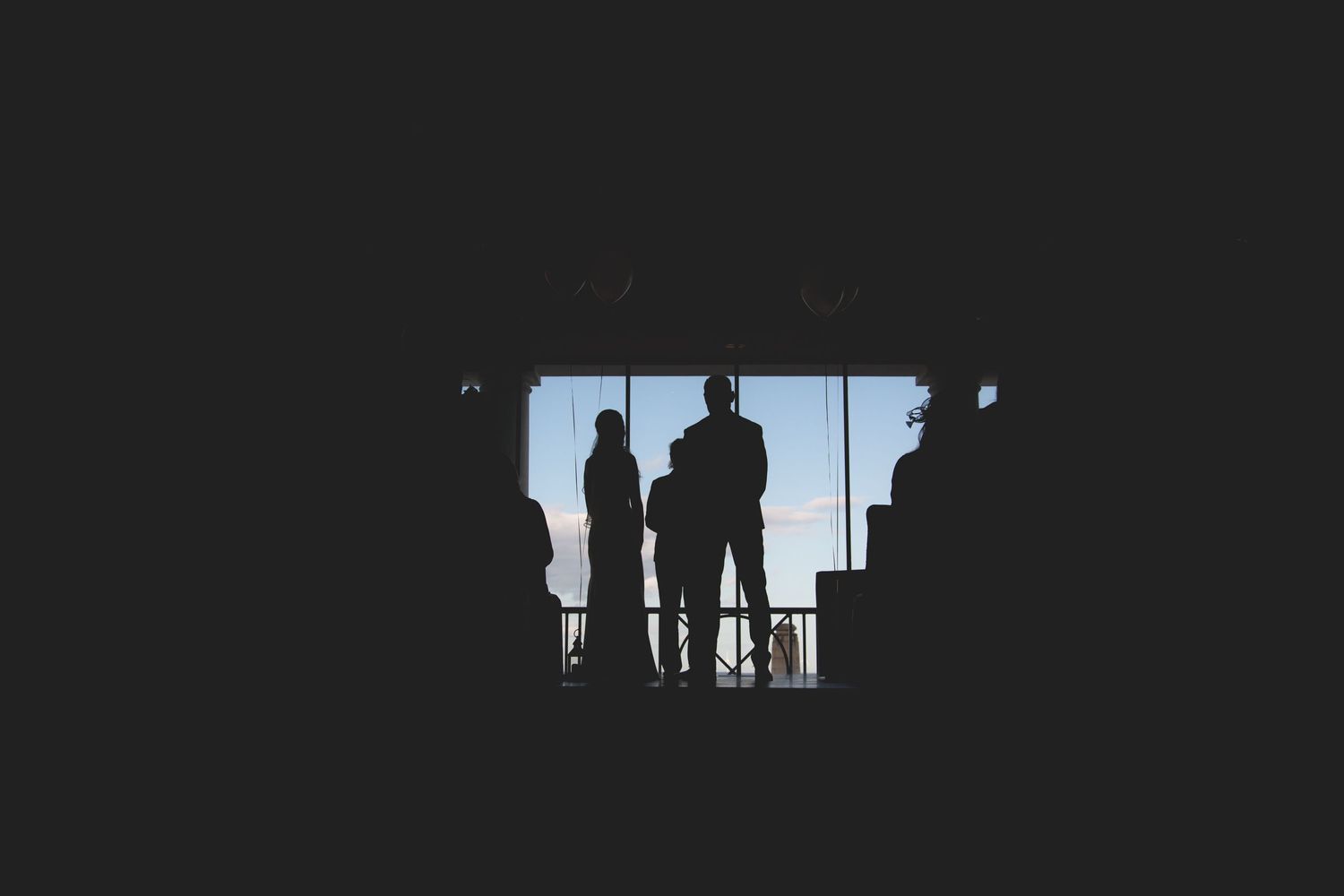 Silhouetted figures seen through window frame in dark interior space.