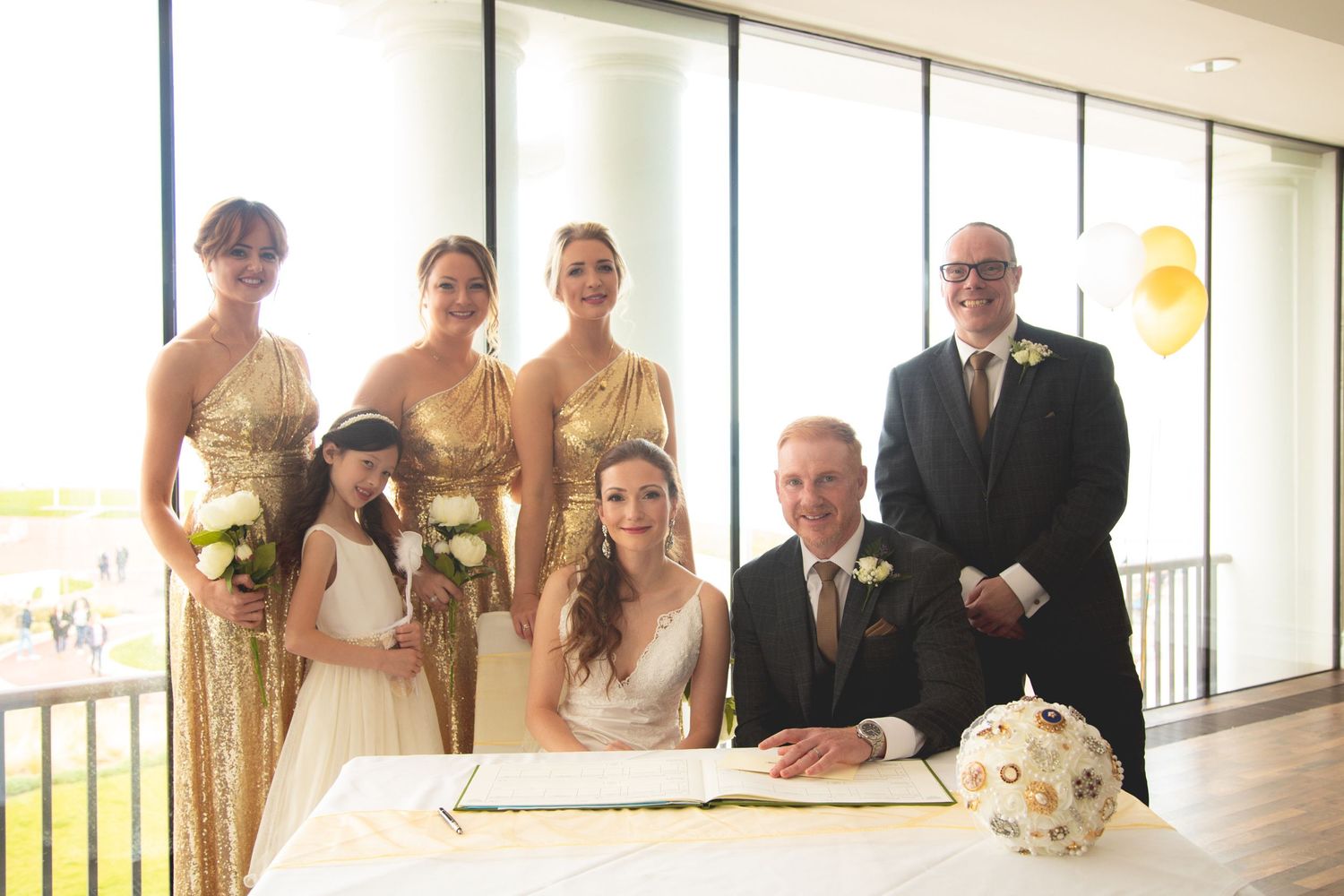 Wedding party gathered around signing table with decorative brooch bouquet.
