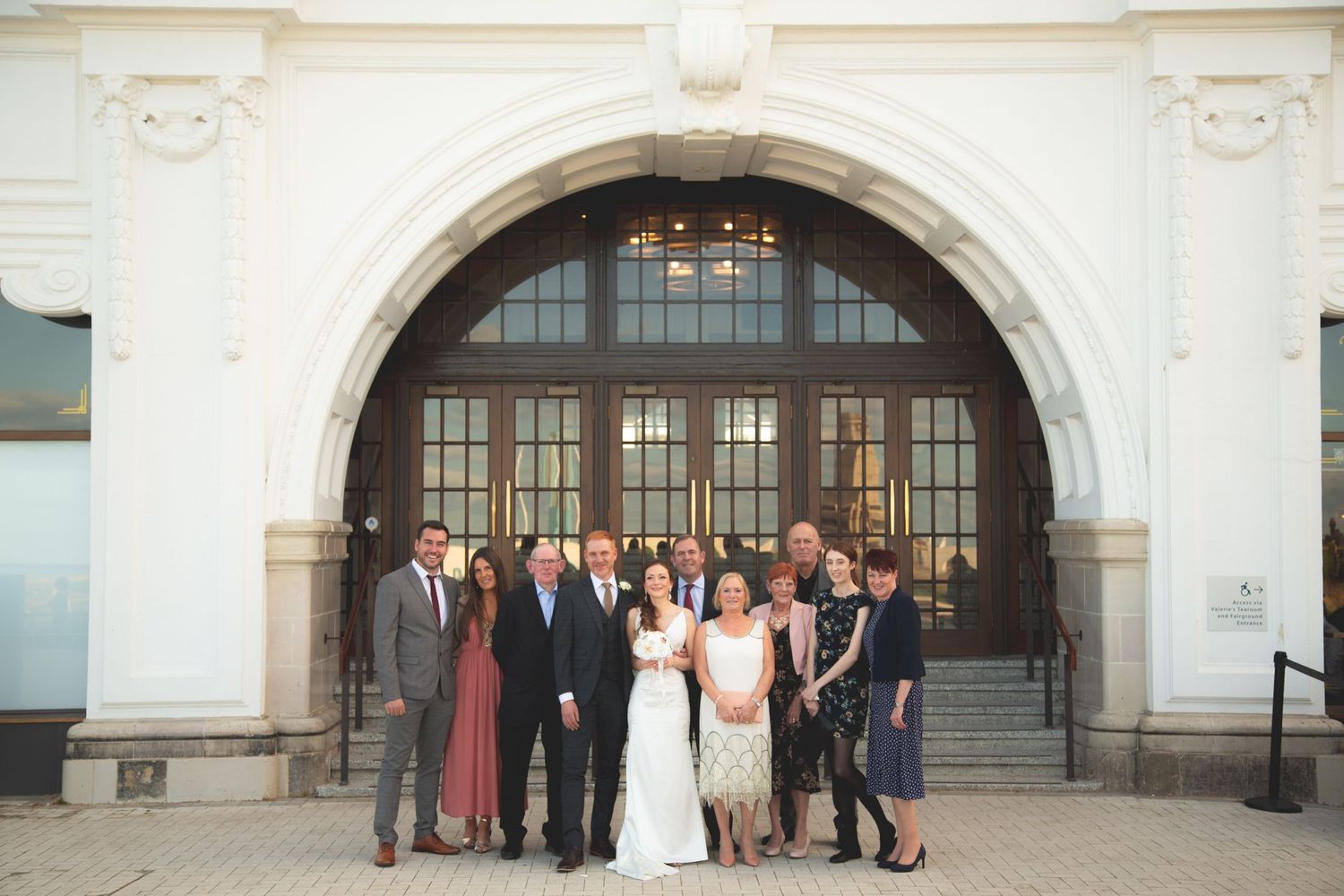 Wedding group portrait in front of grand arched doorway of historic building.