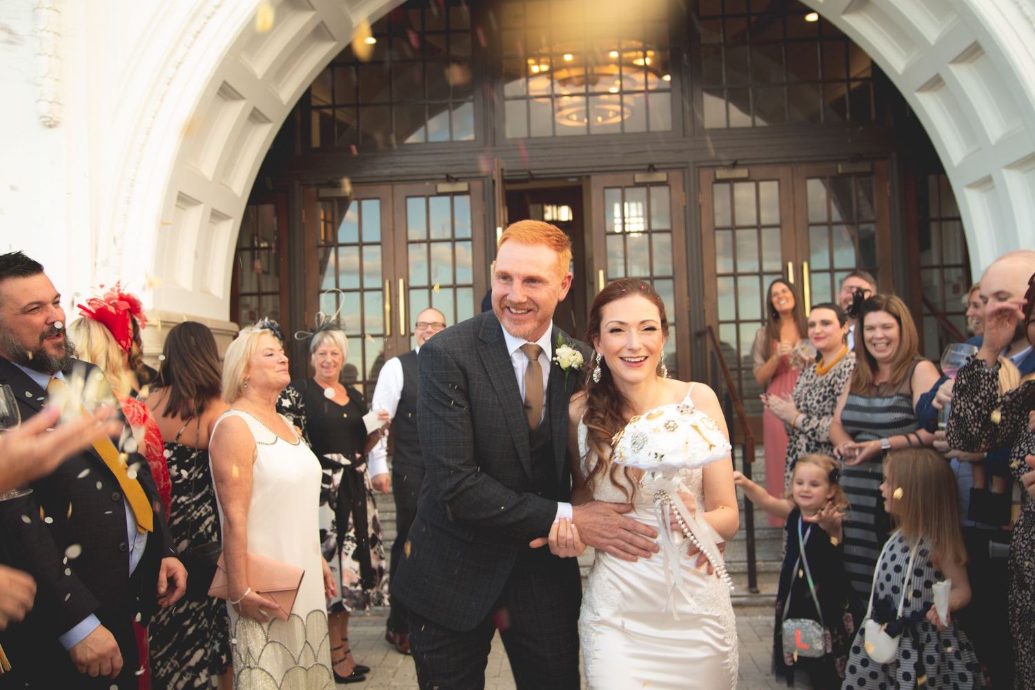 Wedding couple exits through crowd of celebrating guests throwing confetti.