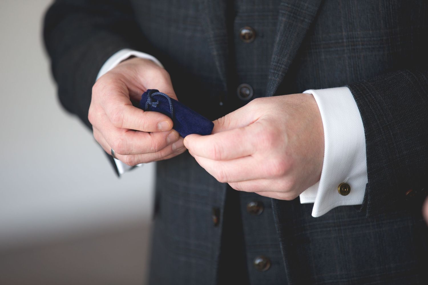 Close-up of hands adjusting a navy blue tie on a gray suit with white cuffed sleeves.