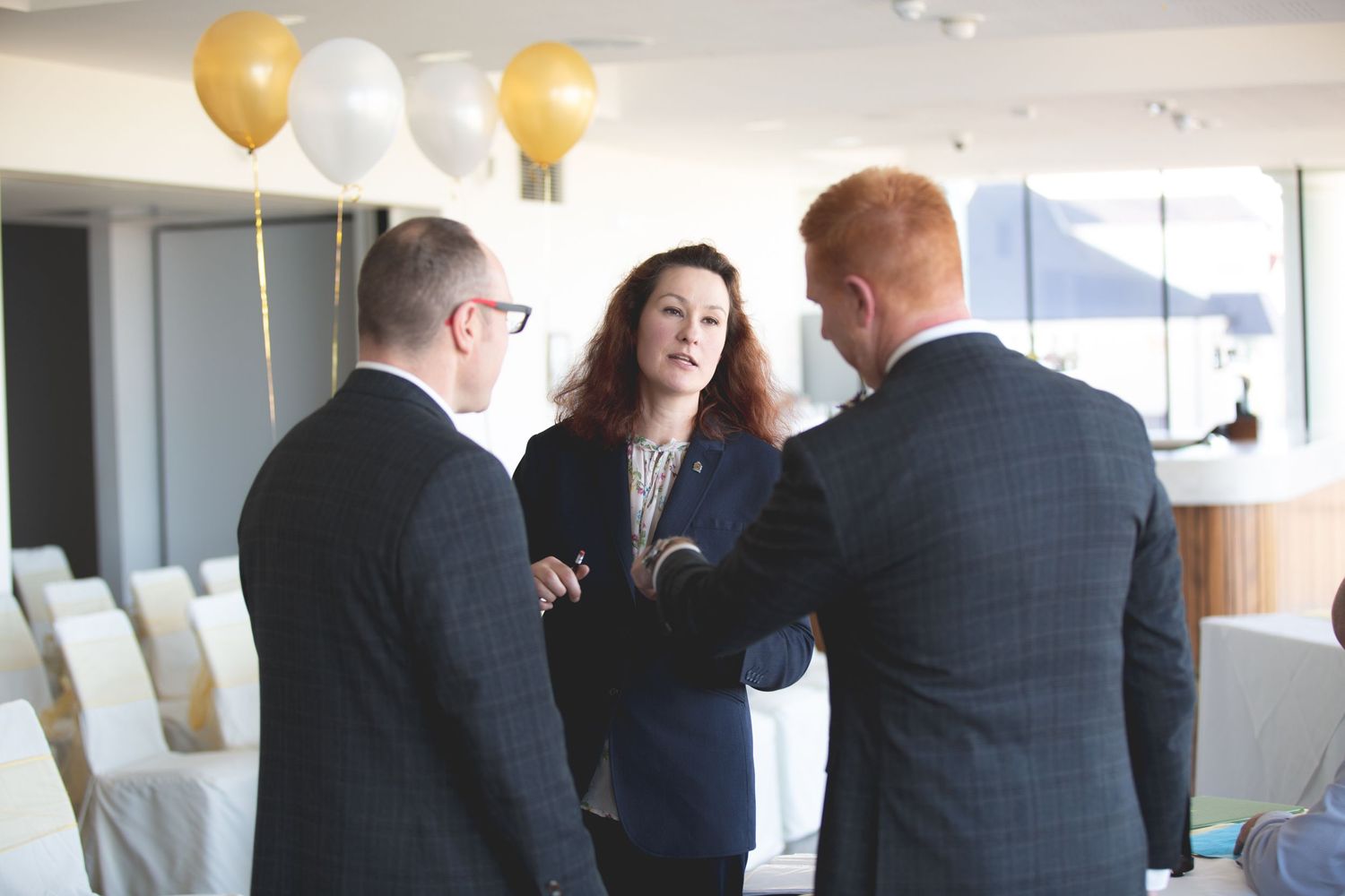 Business meeting with gold and white balloons in a modern office setting.