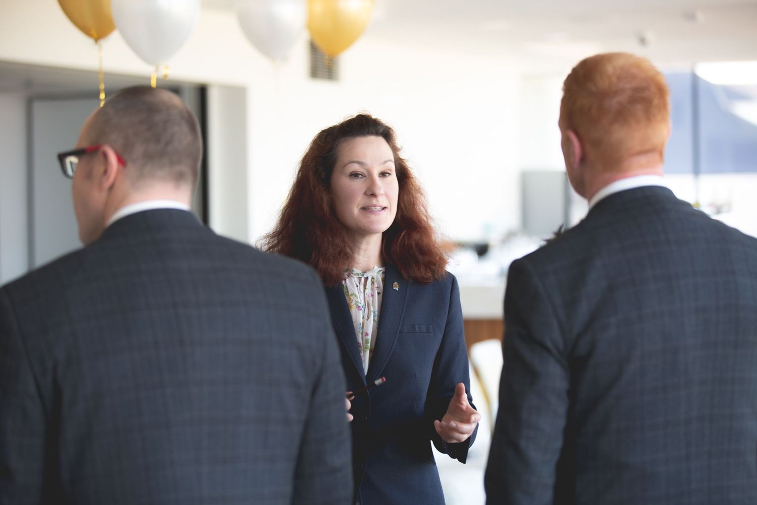 Professional networking conversation in an office space decorated with gold balloons.
