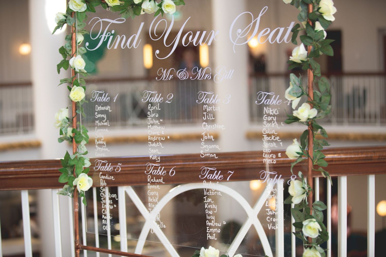 Elegant wedding seating chart decorated with floral garland and cursive text.