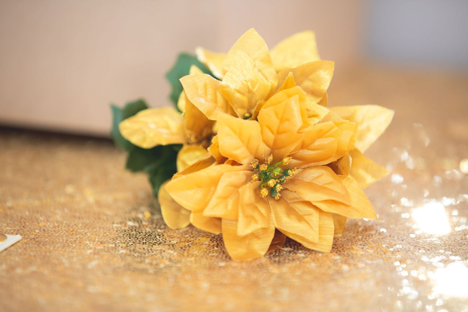 Close-up of a yellow fabric poinsettia flower on a glittery golden surface.