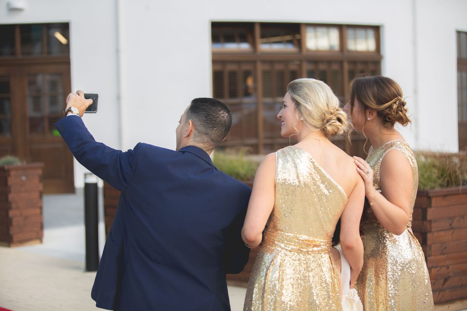 Group taking a selfie wearing formal attire with gold sequined dresses.