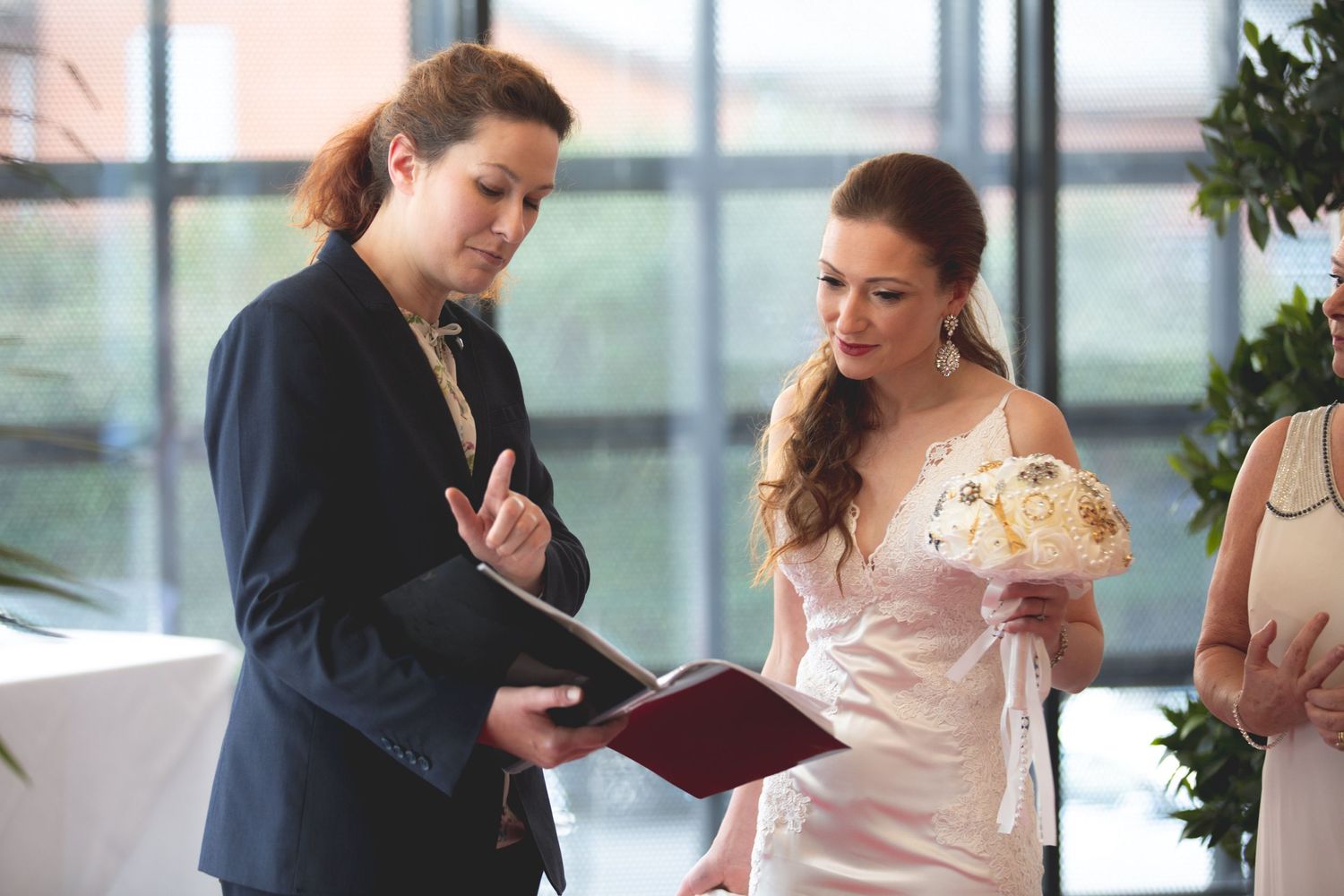 A ceremony officiant reviews paperwork with a bride in a blush pink dress holding a bouquet.
