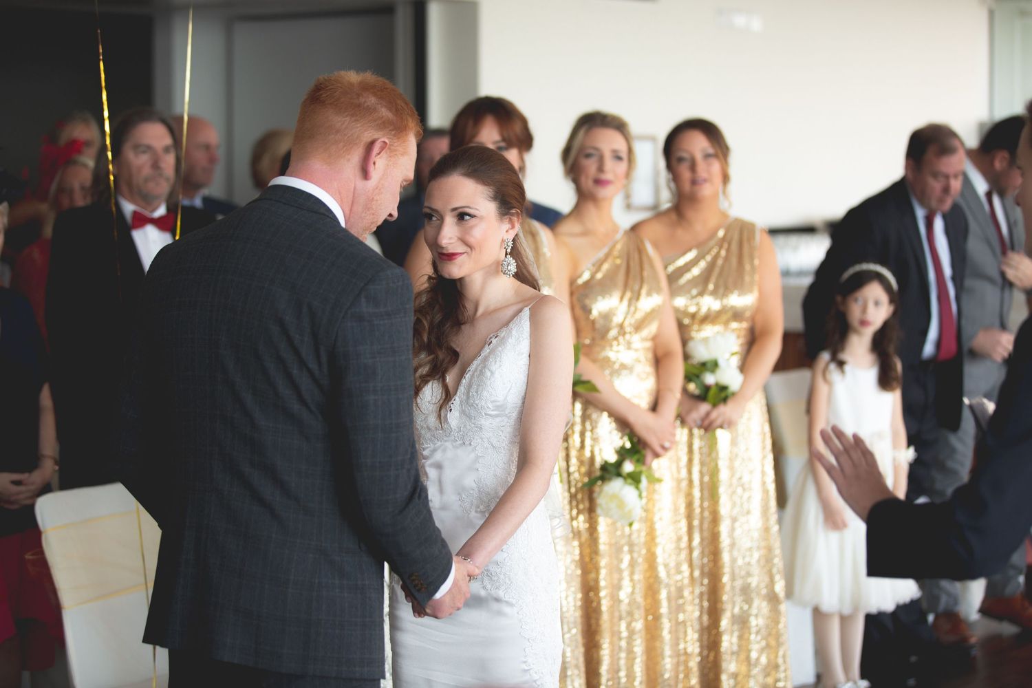 A wedding ceremony with bridesmaids in gold sequined dresses watching from the side.