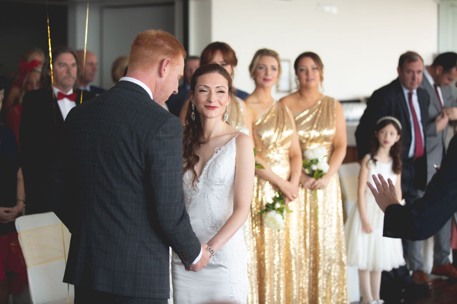 A wedding ceremony with bridesmaids in gold dresses watching the exchange of vows.