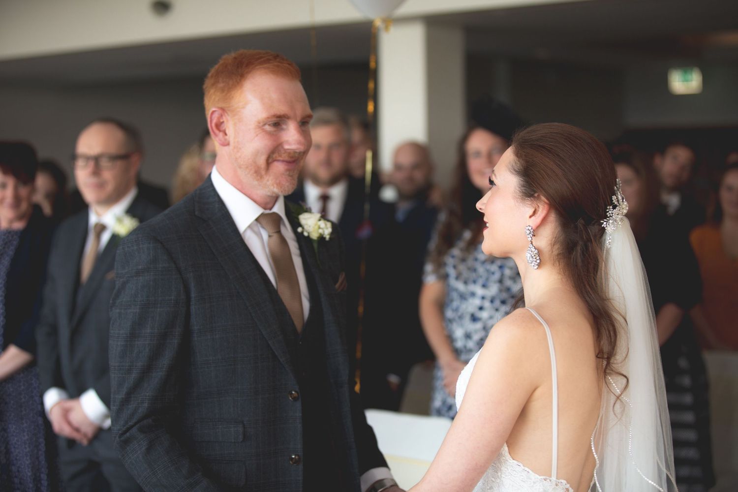 An intimate wedding ceremony moment with guests watching in the background.