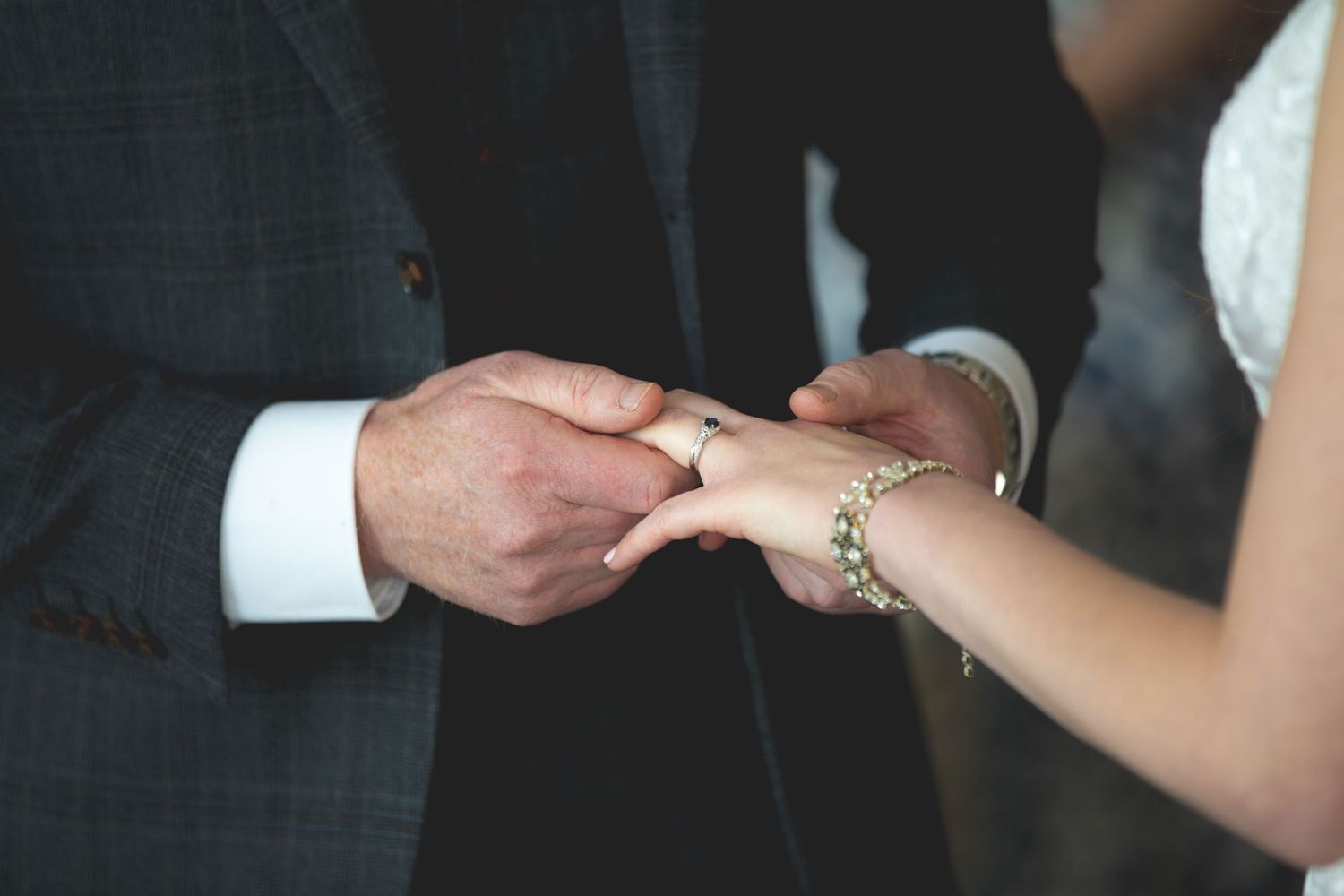 Wedding ring exchange closeup showing hands and delicate jewelry.