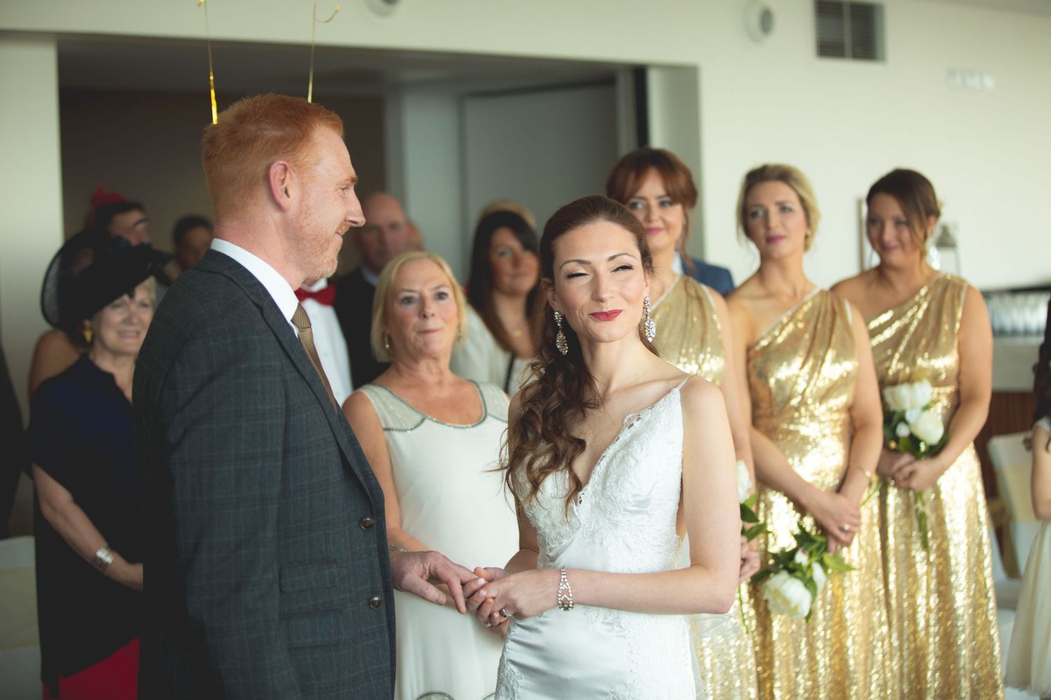 Wedding ceremony with bridesmaids in shimmering gold dresses watching the couple.