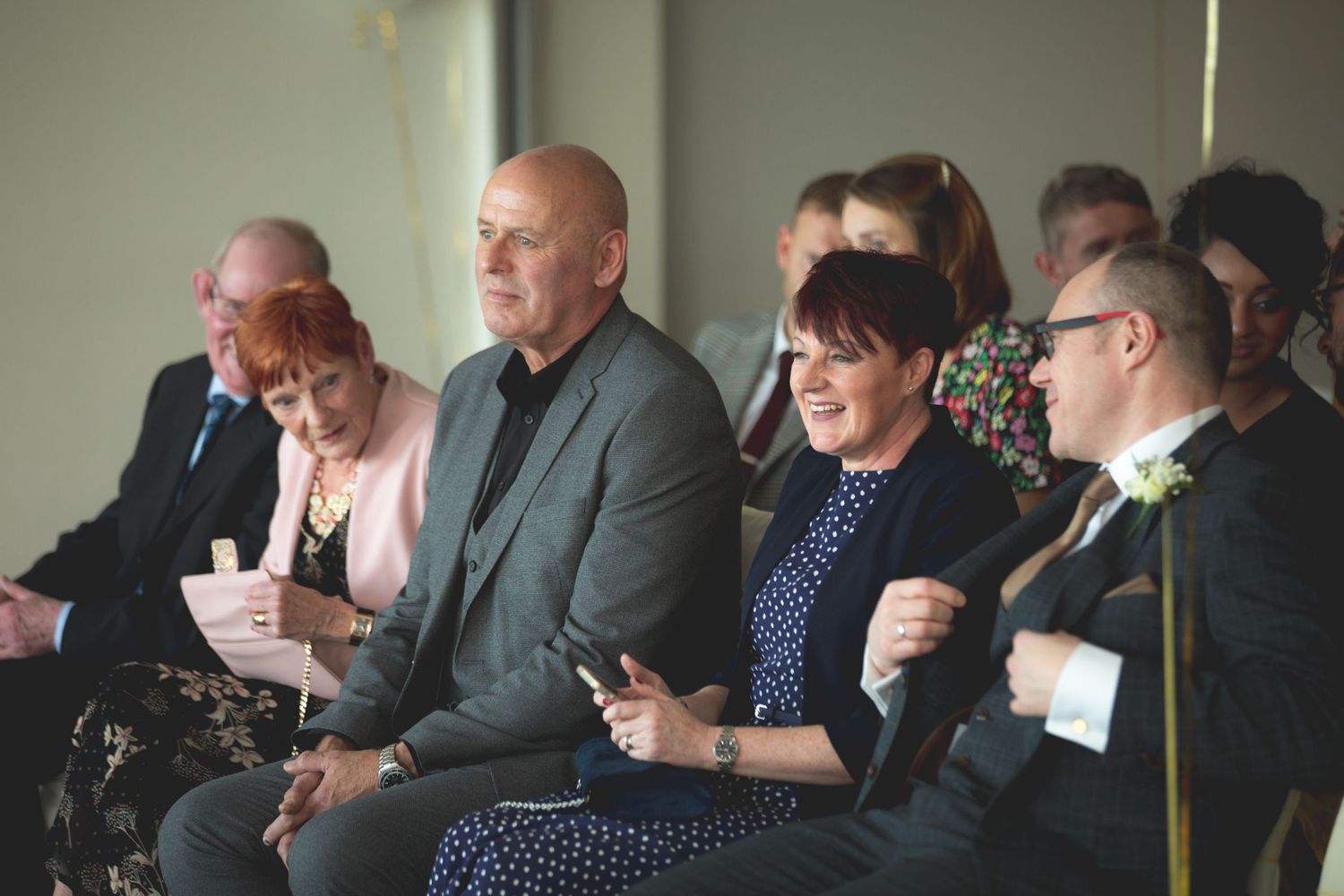 Wedding guests seated and smiling during the ceremony.